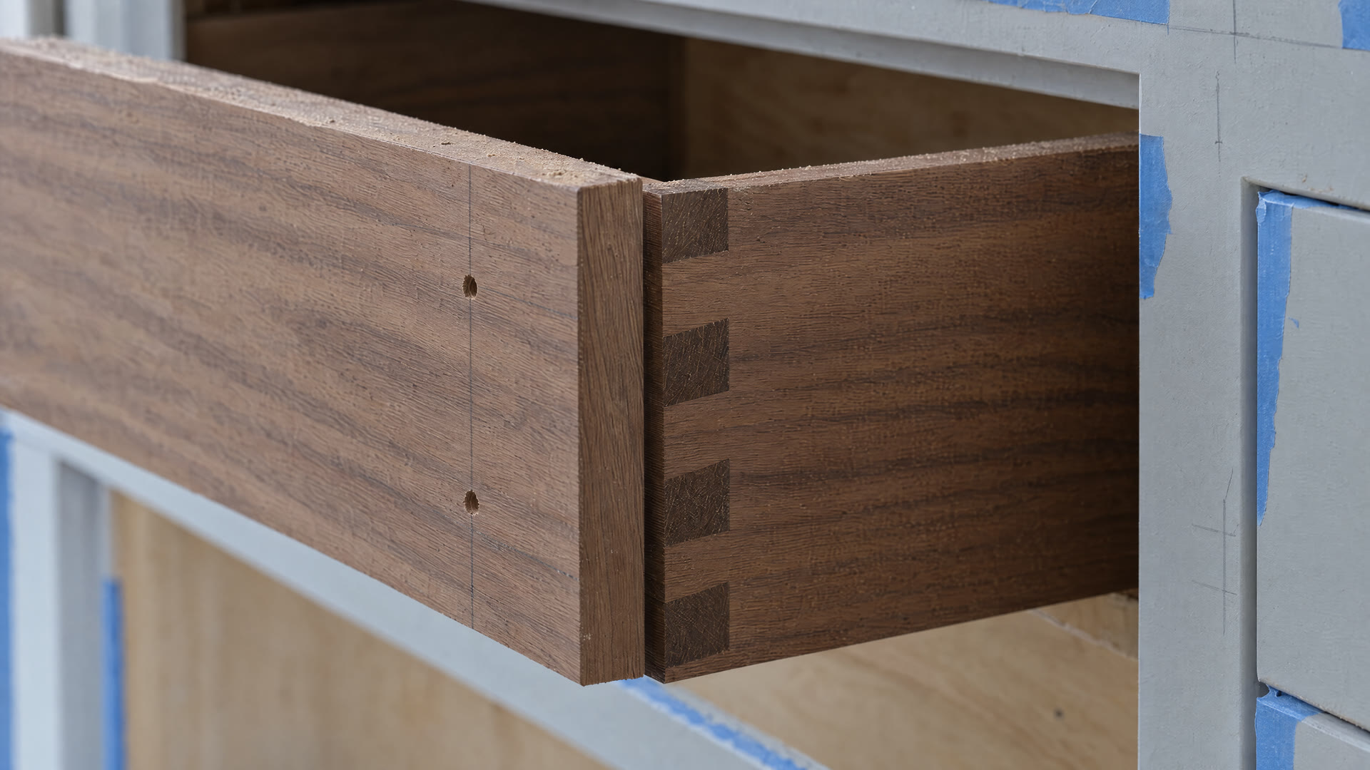 Concept render: the raw walnut drawer box installed before its front, in a primed cabinet with painter's tape