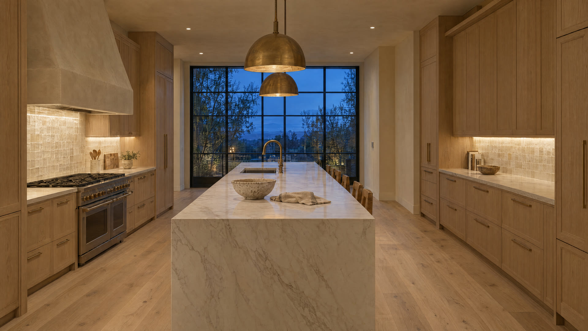 The same kitchen finished: white oak cabinetry, a marble waterfall island and brass pendants
